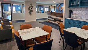 Un hall d’hôtel moderne doté d’espaces détente, d’un comptoir d’accueil et d’un coin cuisine.