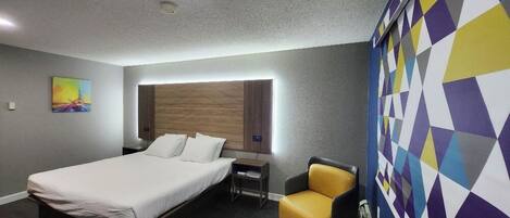 Una habitación de hotel moderna con una cama grande, mesitas de noche, una silla y una pared colorida.