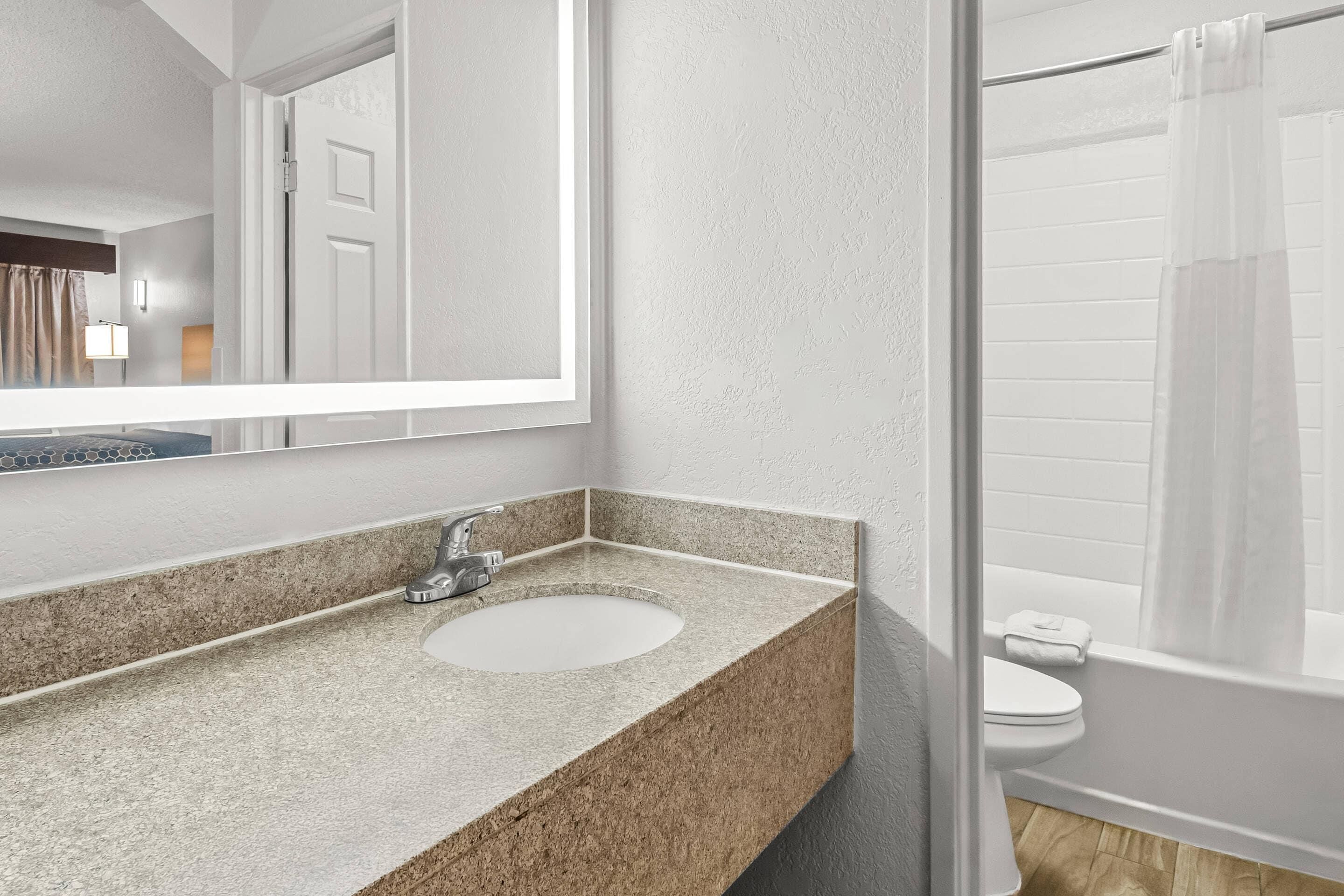 A bathroom with a granite countertop sink, a mirror, and a shower with a curtain.