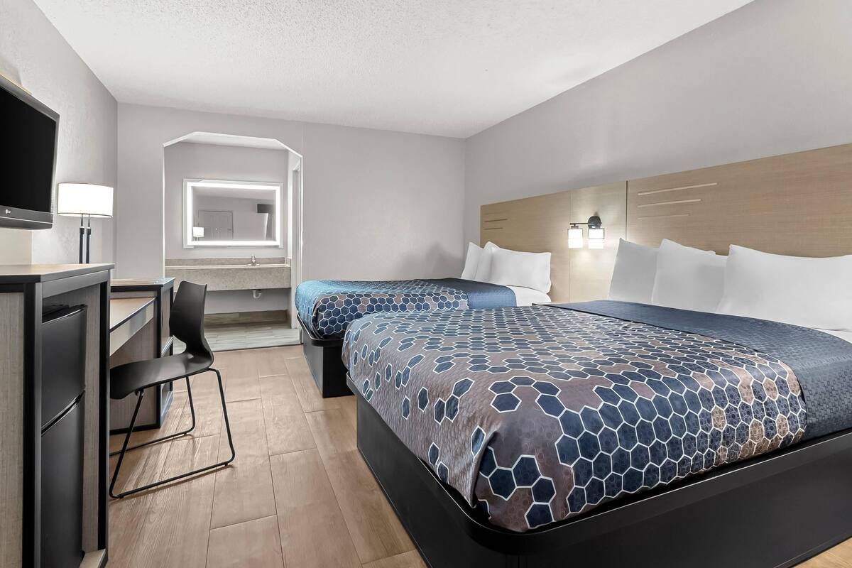 A modern hotel room with two beds, a desk, a chair, and a television.