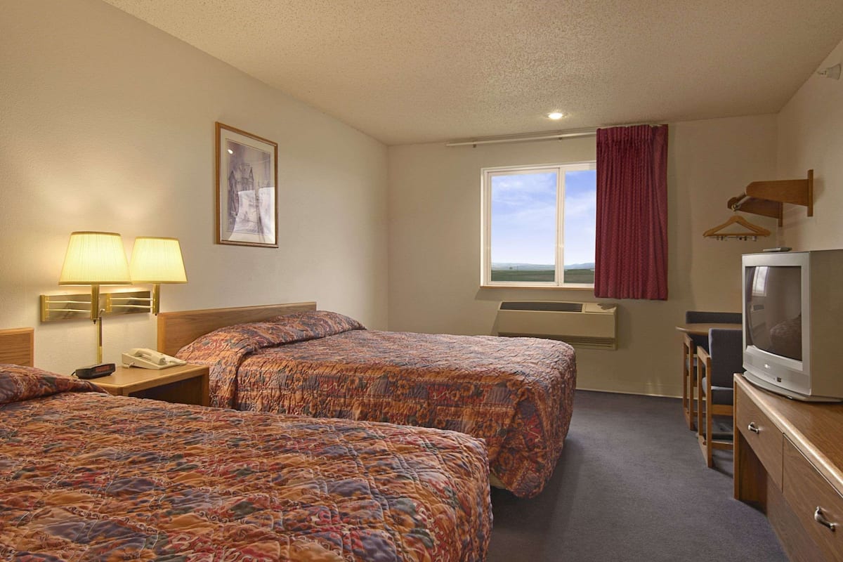 A hotel room with two beds, a television, a desk, and a window with a view.