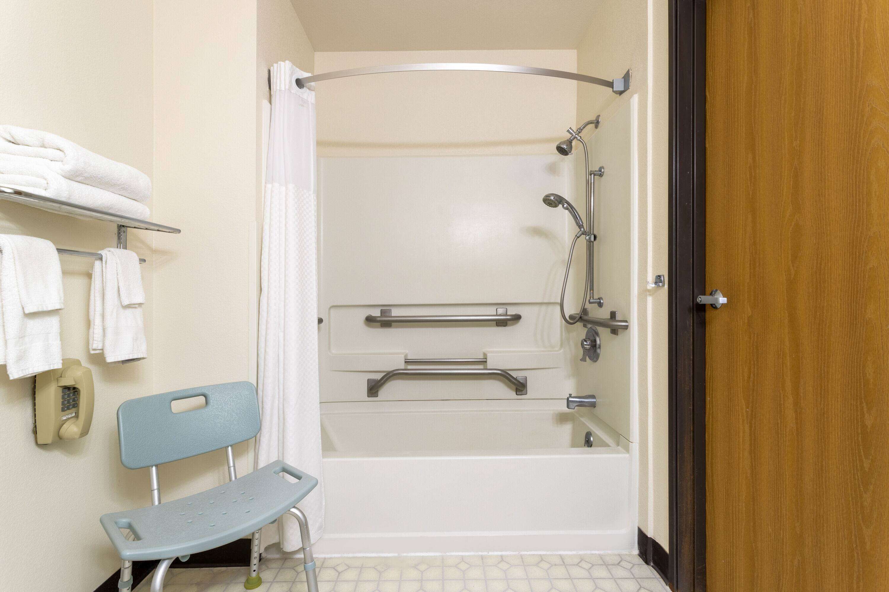 A bathroom with a shower, grab bars, a bench, and a towel rack.