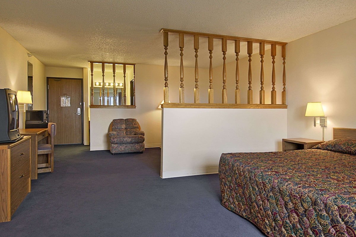 A hotel room with a bed, a desk with a chair, a television, and a mirror.