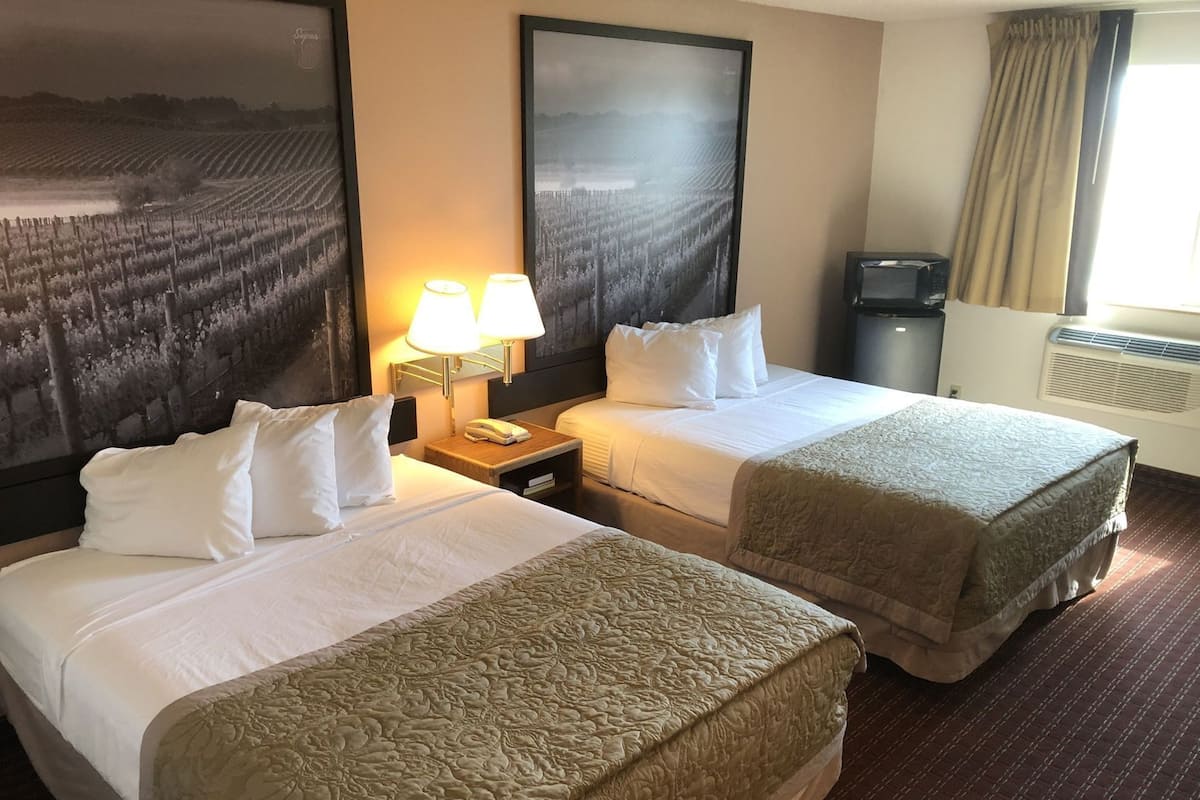 A hotel room with two beds, a nightstand with a lamp, a telephone, and a large framed picture on the wall.