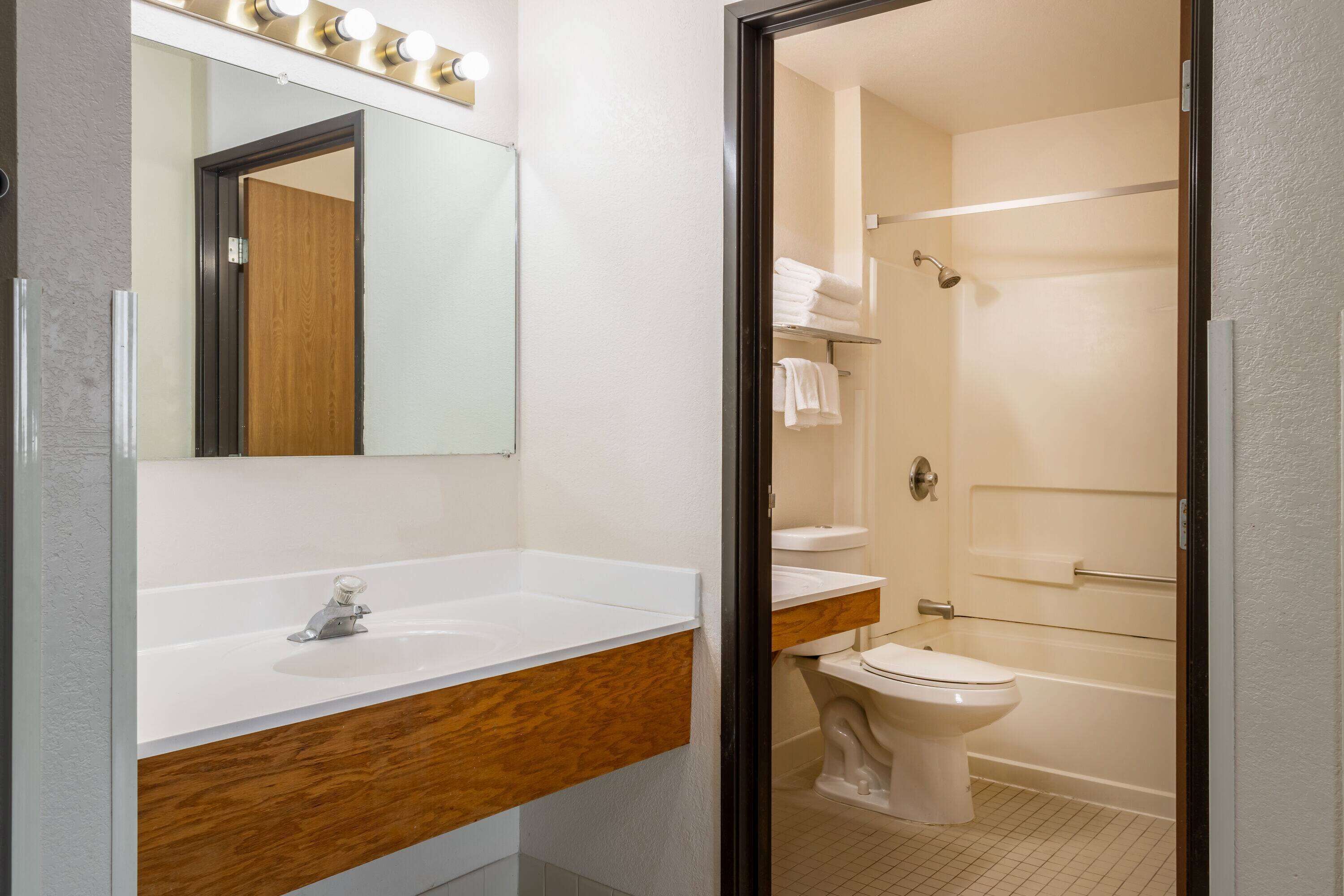 Ein Badezimmer mit einem Holzbadezimmerhocker, einem weißen Waschbecken, einem Spiegel mit Beleuchtung, einer Toilette und einer Duschkabine aus Glas.