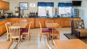 A spacious kitchen with wooden cabinets, a dining area with wooden tables and chairs, a sofa, and a television mounted on the wall. - Super 8 by Wyndham Pendleton (Pendleton)