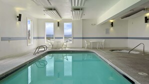 A swimming pool with clear water, surrounded by white chairs and tables, and large windows offering a view of the sky and distant landscape. - Super 8 by Wyndham Pendleton (Pendleton)