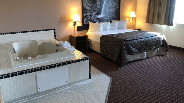 A hotel room with a large bed, a separate bathtub, two bedside lamps, and a large framed picture on the wall. - Super 8 by Wyndham Pendleton (Pendleton)