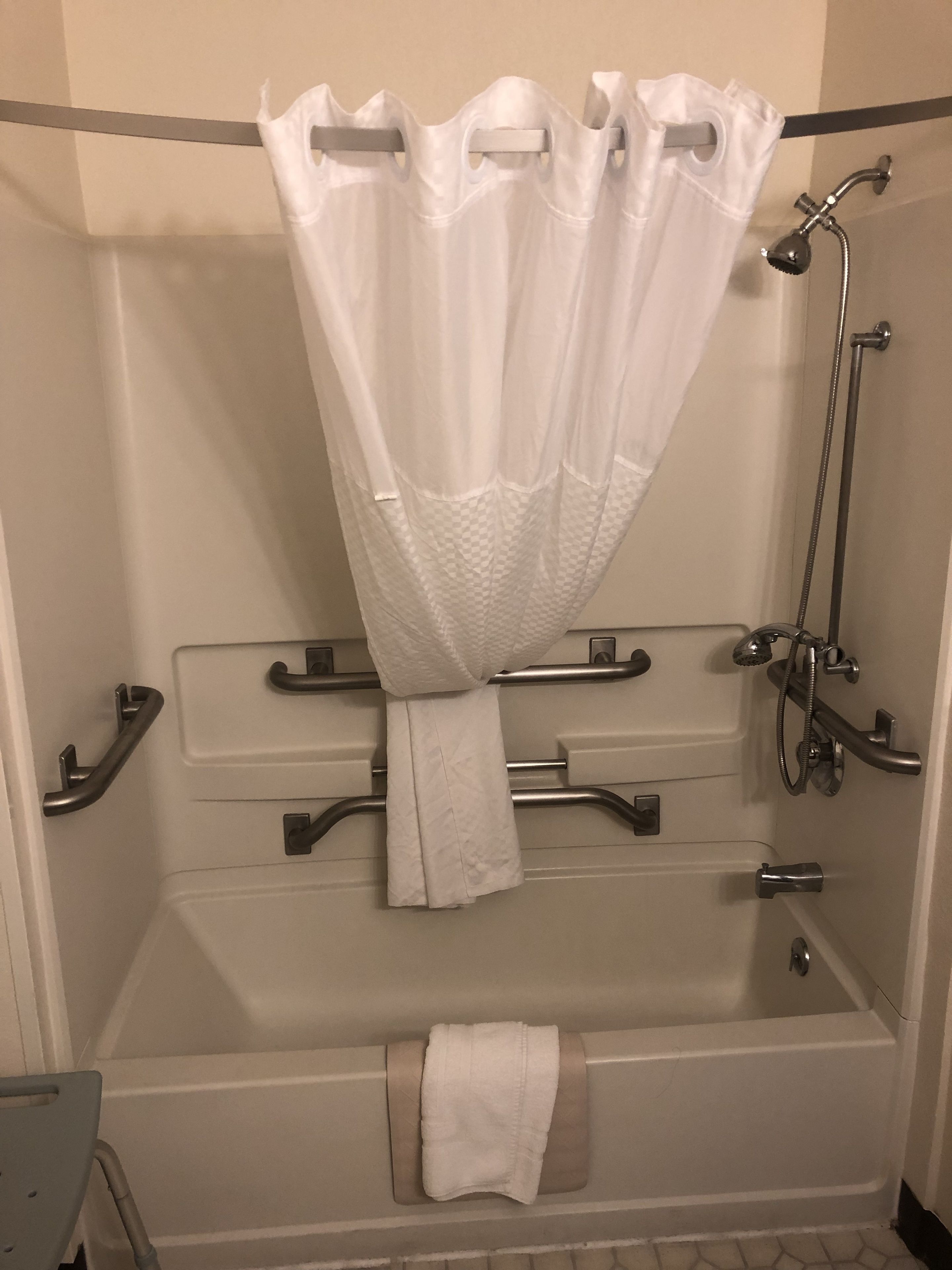 Un baño de hotel estándar con bañera, ducha y barras de apoyo.