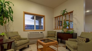 A living room with two green armchairs, a glass-top coffee table, a wooden cabinet, and a large window with a view of buildings. - Super 8 by Wyndham Pendleton (Pendleton)