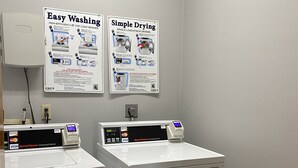A laundry area with two washers and dryers, a poster explaining their use, and a payment terminal. - AmericInn by Wyndham Mauston (Mauston)