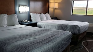 A hotel room with two beds, a nightstand with a phone, a lamp, and a window with a view of the beach. - AmericInn by Wyndham Mauston (Mauston)