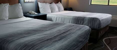 Une chambre d’hôtel avec deux lits, une table de chevet avec un téléphone, une lampe et une fenêtre donnant sur la plage.