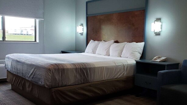 A hotel room with a large bed, a bedside table with a phone, and a window with a view of the outside. - AmericInn by Wyndham Mauston (Mauston)