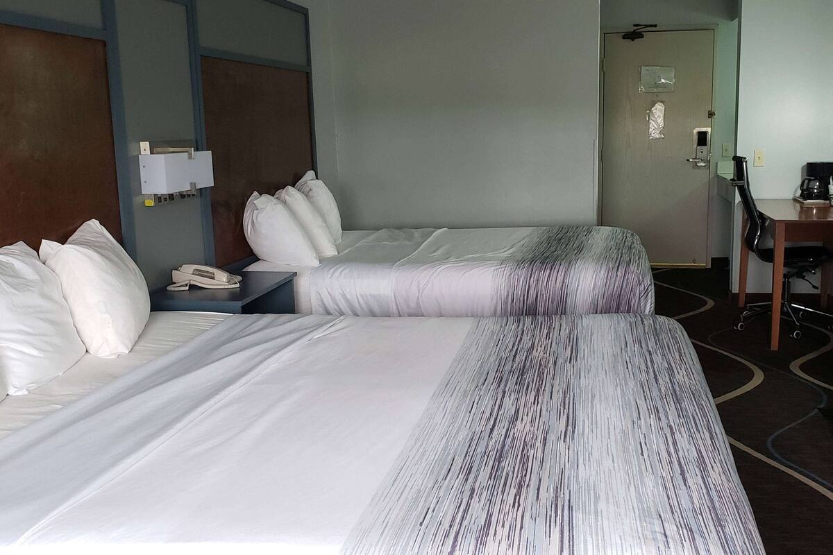 A hotel room with two beds, a desk, a chair, and a coffee maker.