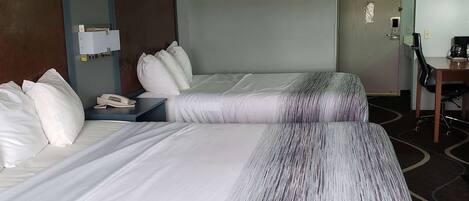 A hotel room with two beds, a desk, a chair, and a coffee maker.