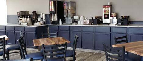 A café with wooden tables and blue chairs, a coffee machine, and a sign indicating breakfast hours.