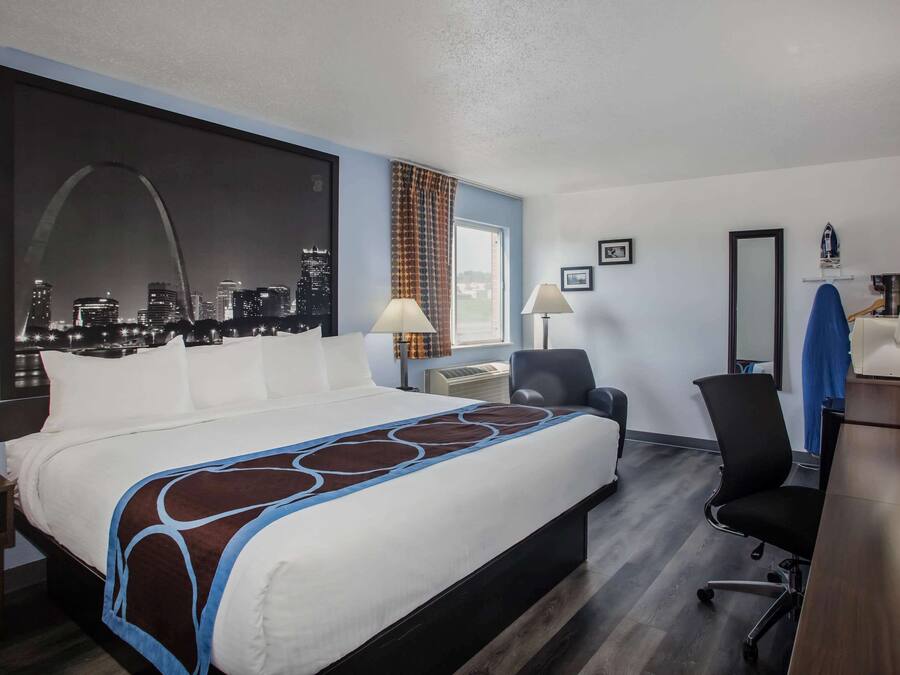 A hotel room with a large bed, a desk, a chair, a TV, and a cityscape view.