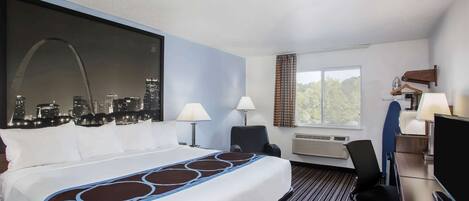 A hotel room with a large bed, two bedside lamps, a desk with a television, and a view of a city skyline.