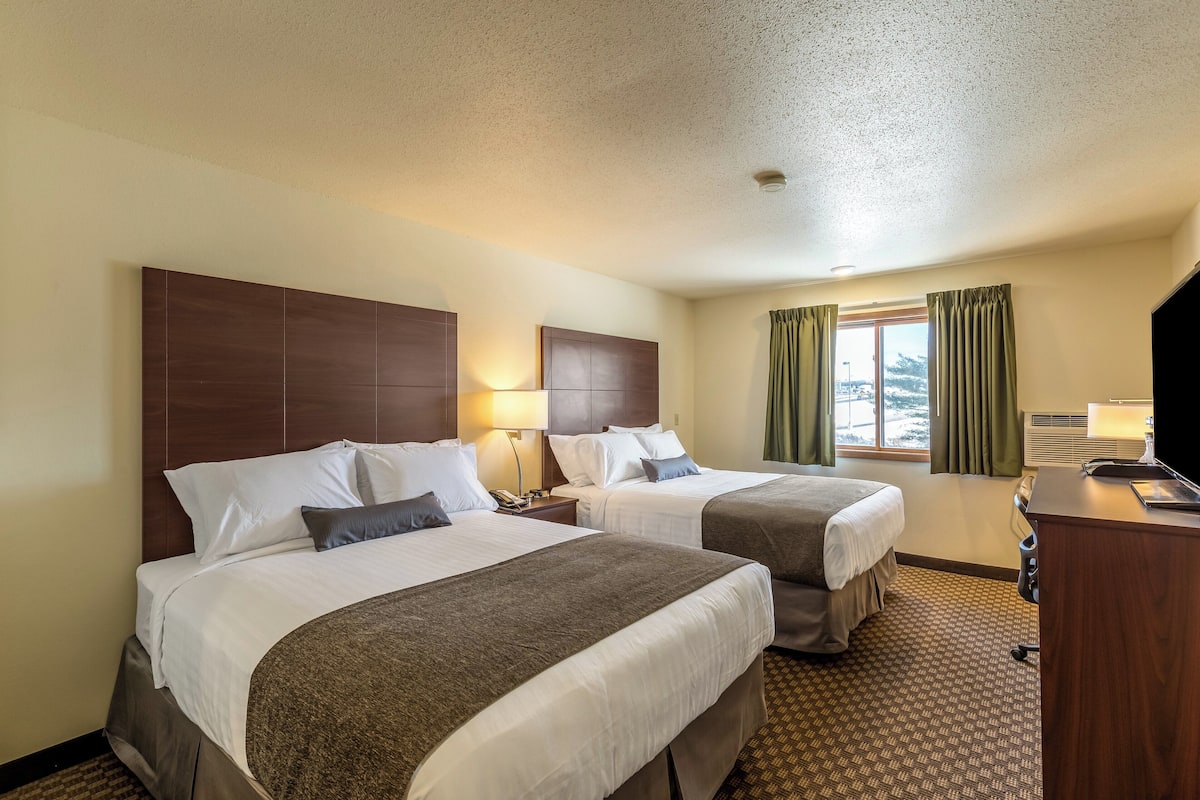 Quarto de hotel com duas camas, uma escrivaninha e uma janela com cortinas.