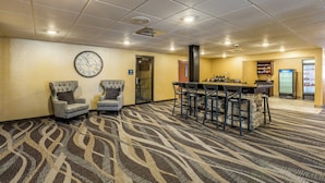 A hotel lobby with a bar area, two armchairs, a clock, and a patterned carpet.