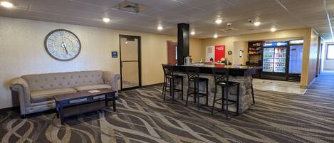 A hotel lobby with a sofa, a coffee bar, a clock, and vending machines.