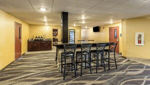 A conference room with a long table and four chairs, a bar area with a refrigerator, and a vending machine.