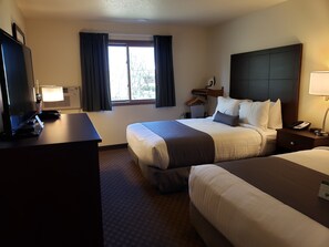 A hotel room with a bed, bedside table, lamp, and a TV. - Cobblestone Inn & Suites Merrill (Merrill)