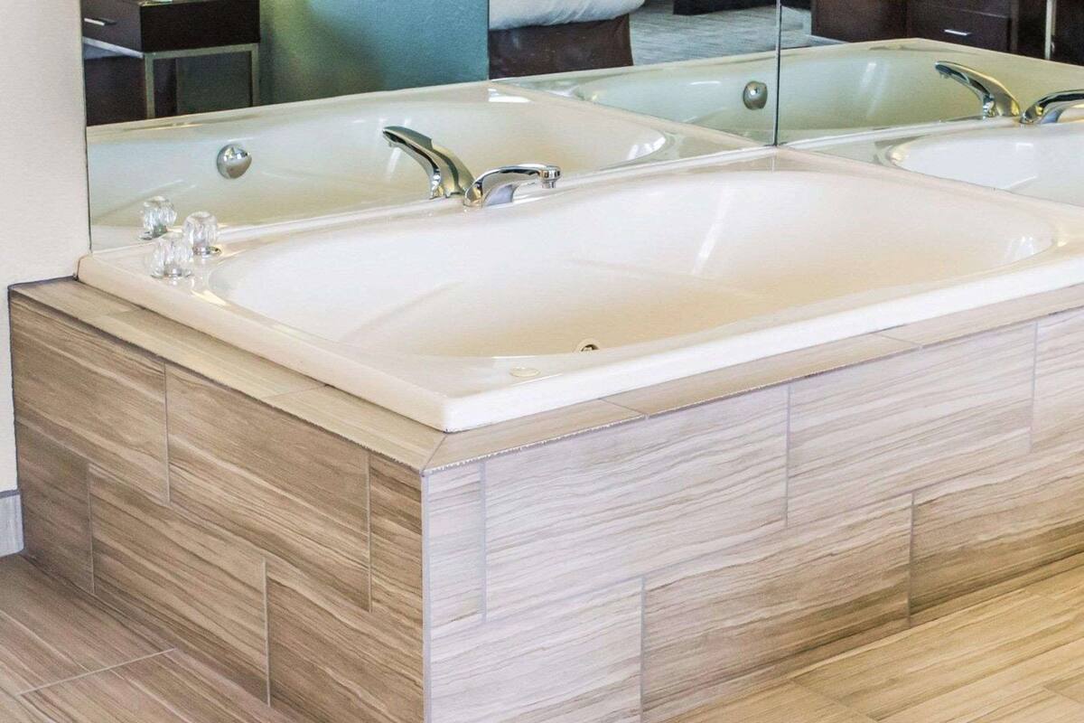 A modern bathroom with a large freestanding bathtub, a mirror above the sink, and wooden flooring.