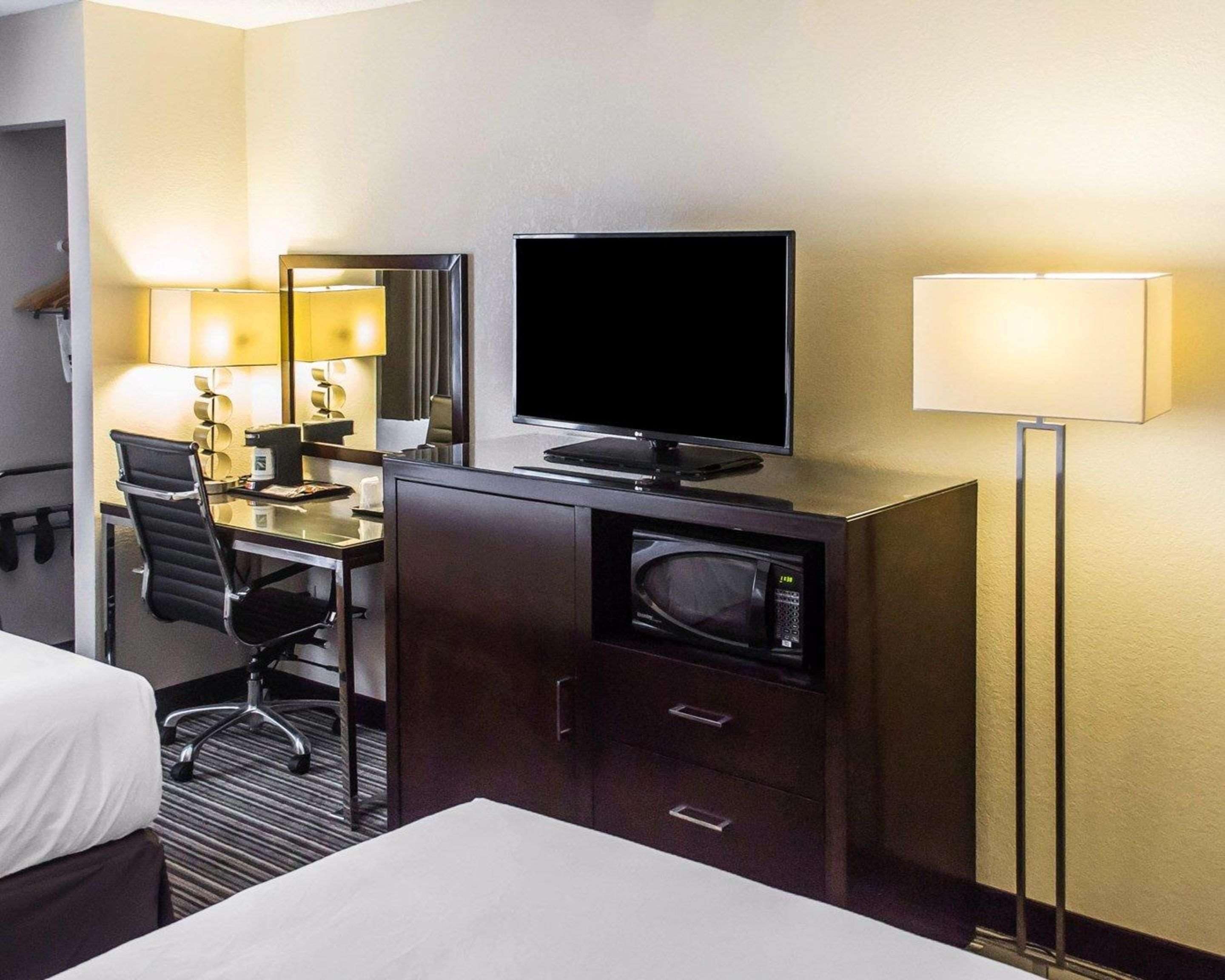 A hotel room with a bed, a desk with a computer and a flat-screen TV, a microwave, and a bedside lamp.