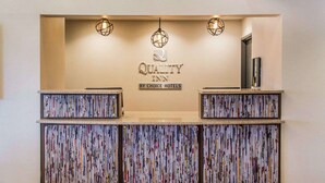 A reception desk with a 'Quality Inn' sign, three pendant lights, and a bookshelf filled with magazines. - Quality Inn Streetsboro - Kent (Streetsboro)