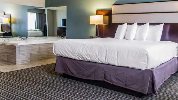 A hotel room with a large bed, a separate bathroom with a vanity, a mirror, and a nightstand with a lamp. - Quality Inn Streetsboro - Kent (Streetsboro)