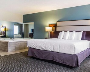 A hotel room with a large bed, a separate bathroom with a vanity, a mirror, and a nightstand with a lamp.