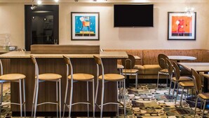 A modern bar area with a counter, bar stools, and a sofa. There are framed artworks on the walls and a flat-screen TV mounted above the counter. - Quality Inn Streetsboro - Kent (Streetsboro)