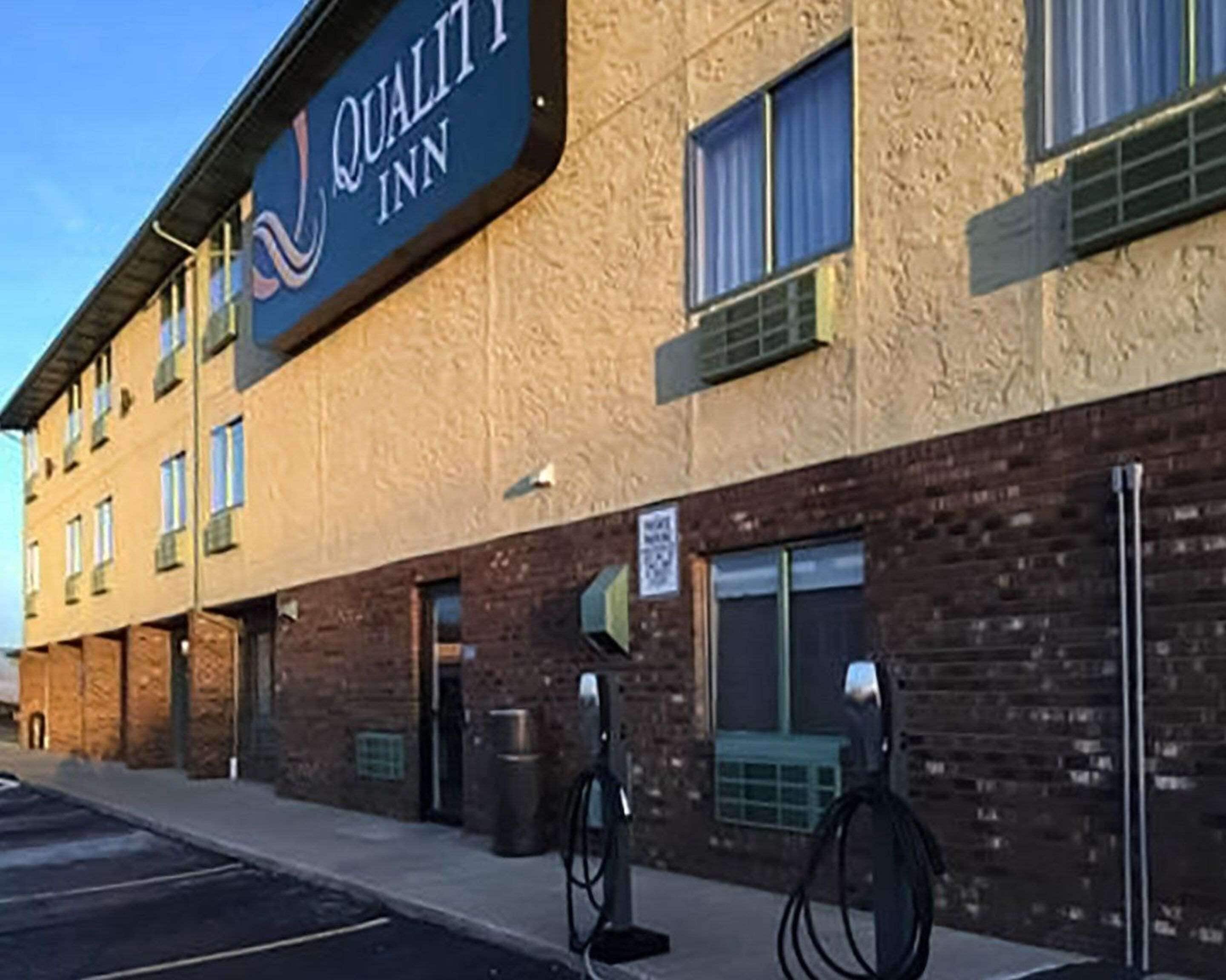 A hotel exterior with a sign reading "Quality Inn." There are two gas pumps on the sidewalk.