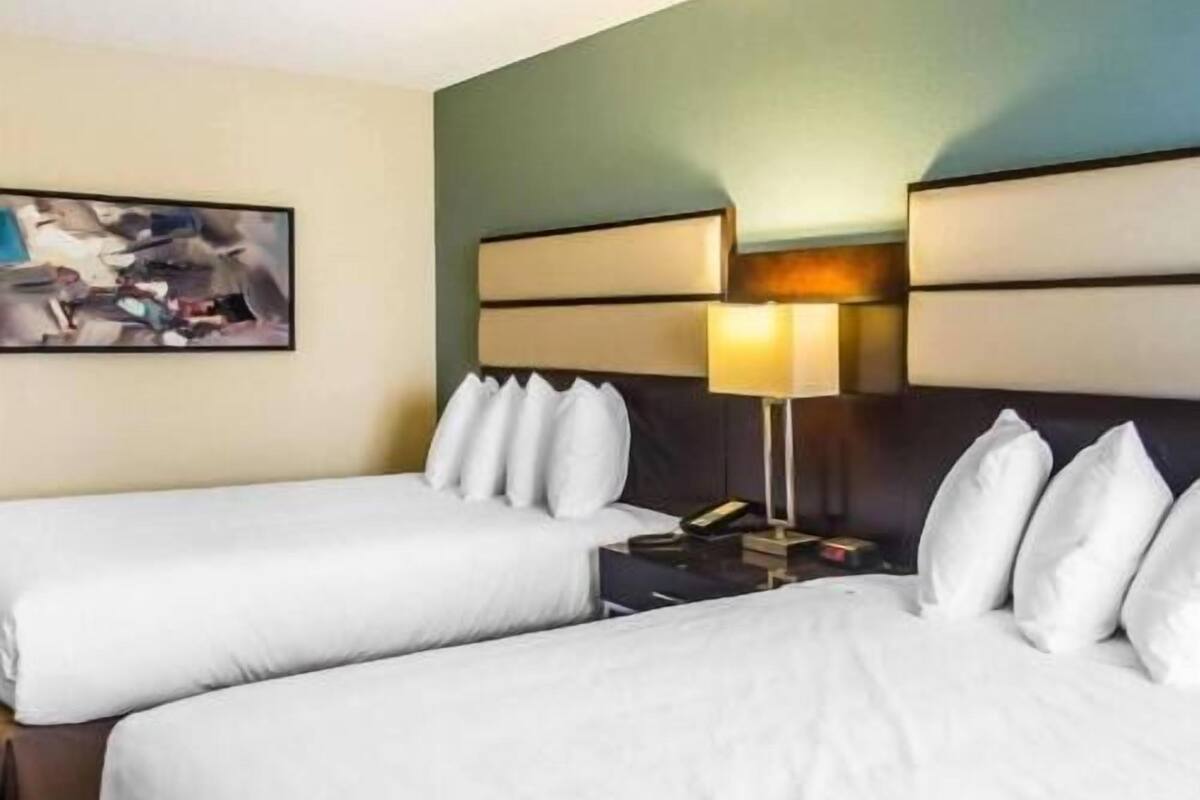 A hotel room with two beds, a nightstand, a lamp, and a painting on the wall.