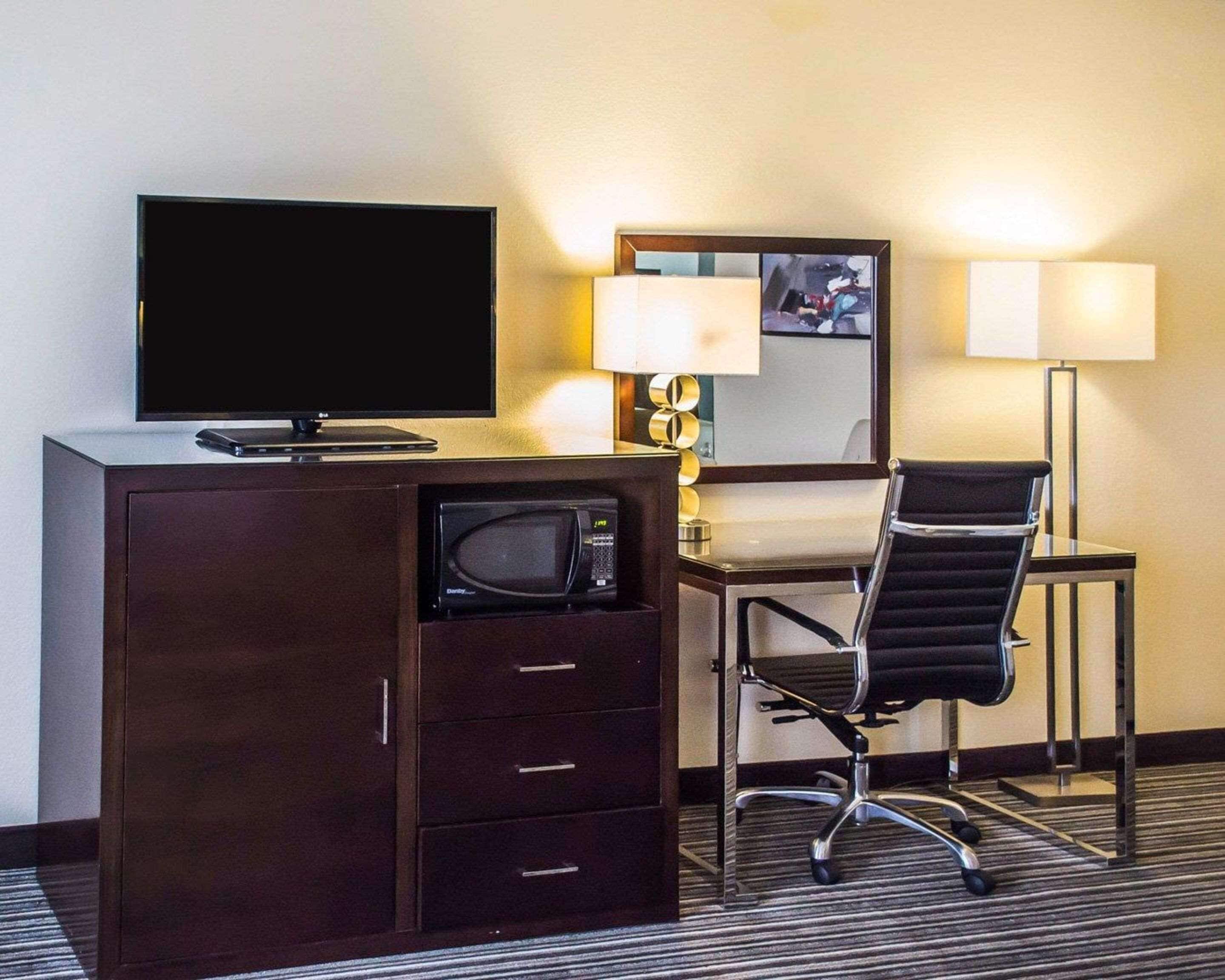 Habitación de hotel con televisión de pantalla plana, microondas, escritorio con silla y dos lámparas.