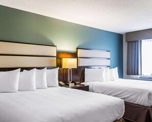 A hotel room with two beds, a nightstand with a lamp, and a window with curtains.