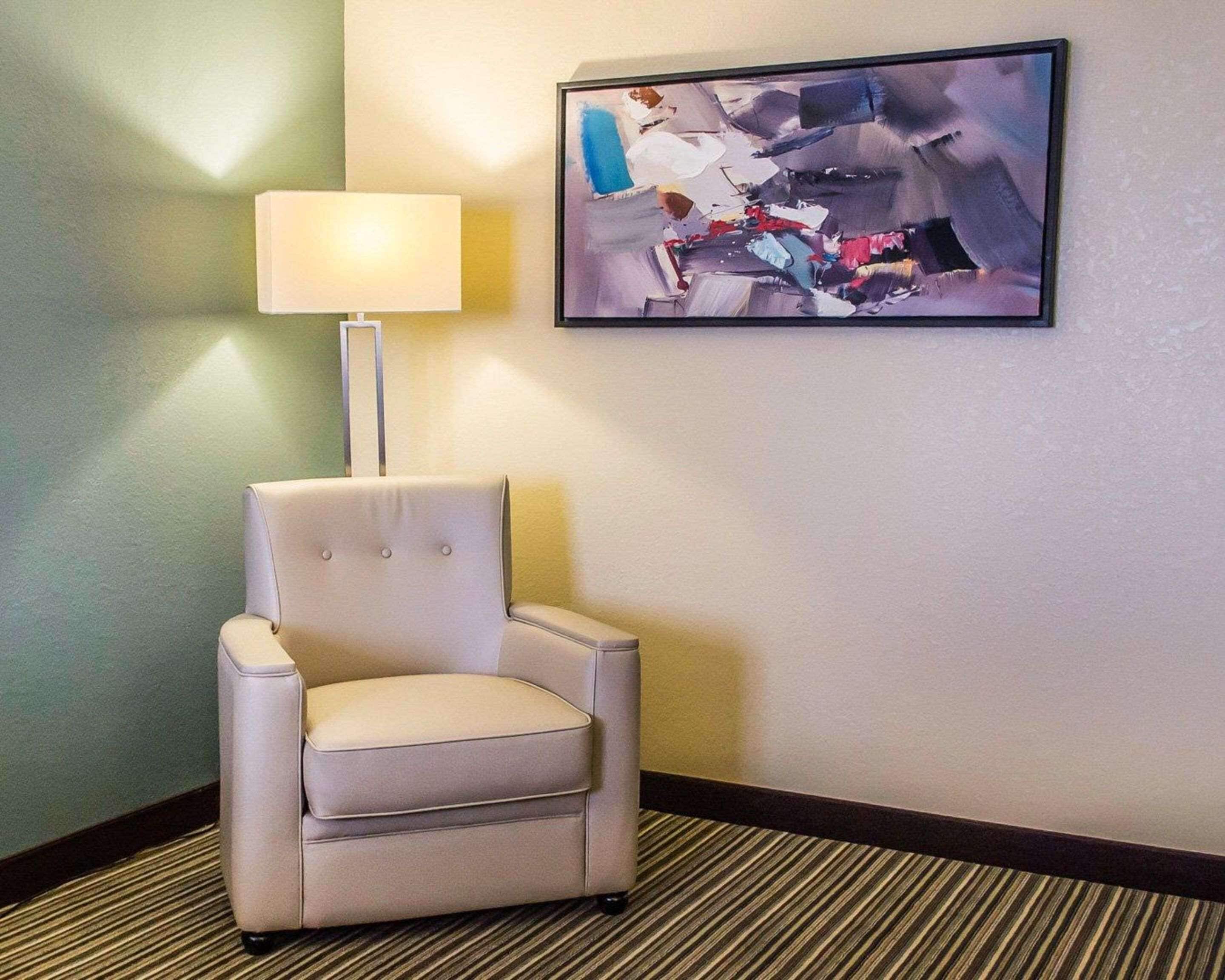 A corner room with a white armchair, a floor lamp, and a large abstract painting on the wall.
