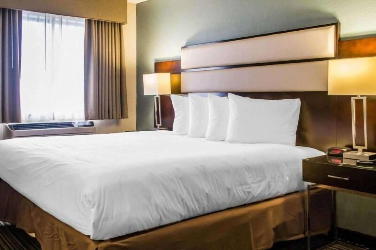 A hotel room with a large bed, a bedside table, a lamp, and a window with curtains.