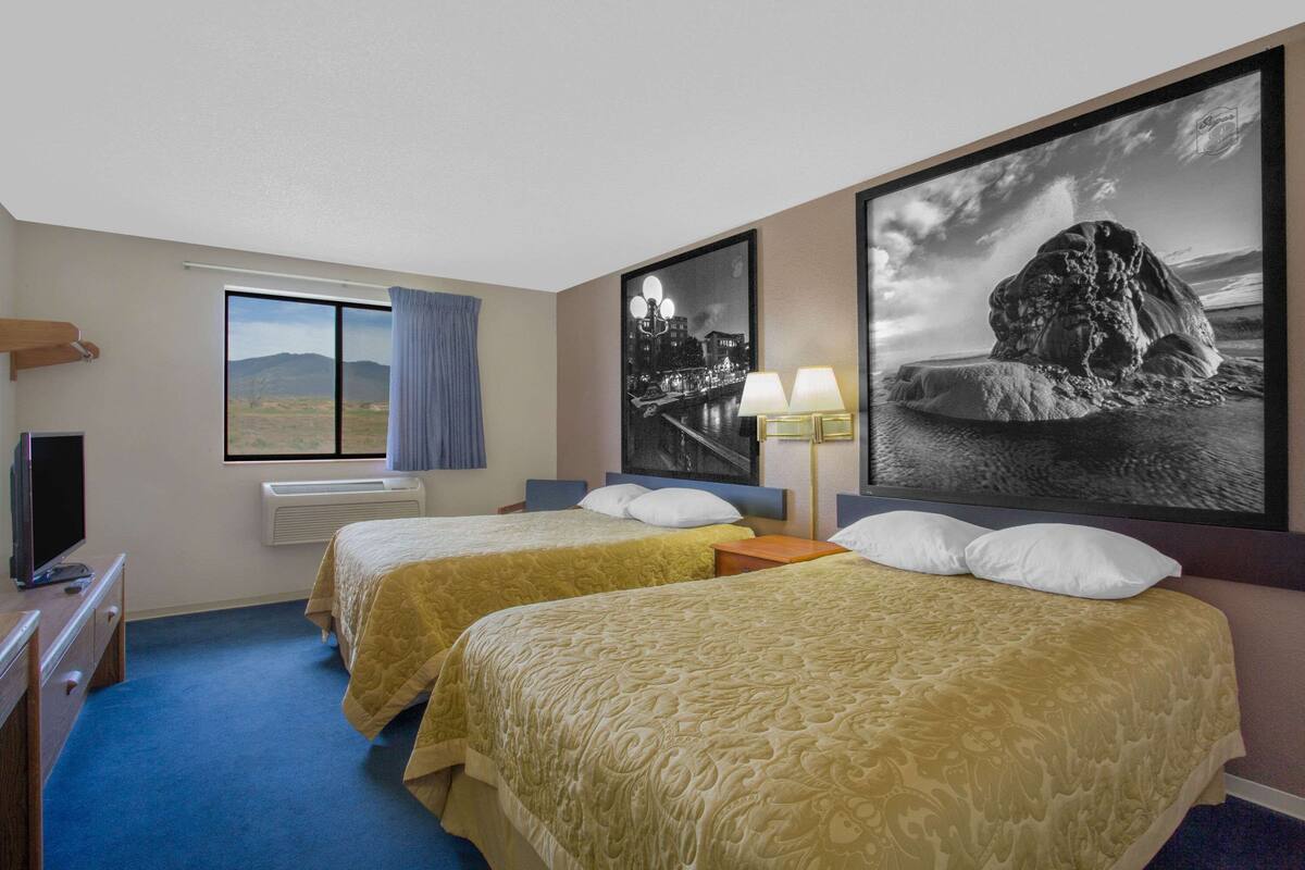 Une chambre d’hôtel avec deux lits, une télévision, une fenêtre donnant sur les montagnes et deux grandes images encadrées accrochées au mur.