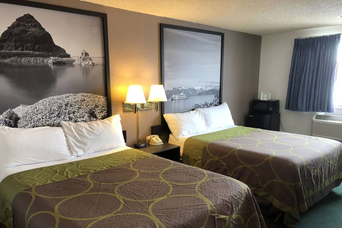 Une chambre d’hôtel avec deux lits, une table de chevet avec une lampe, un téléphone et un climatiseur fixé au mur.