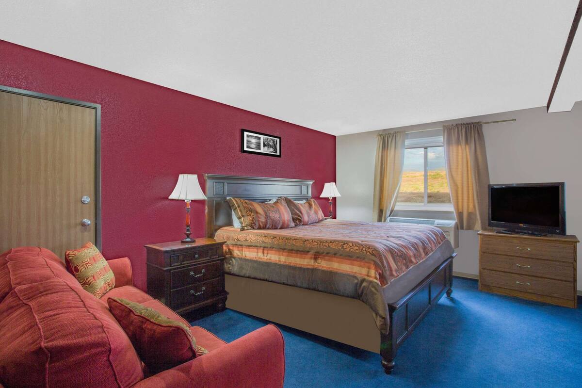 Une chambre à coucher avec un lit, une télévision, une commode et une fenêtre avec des rideaux.