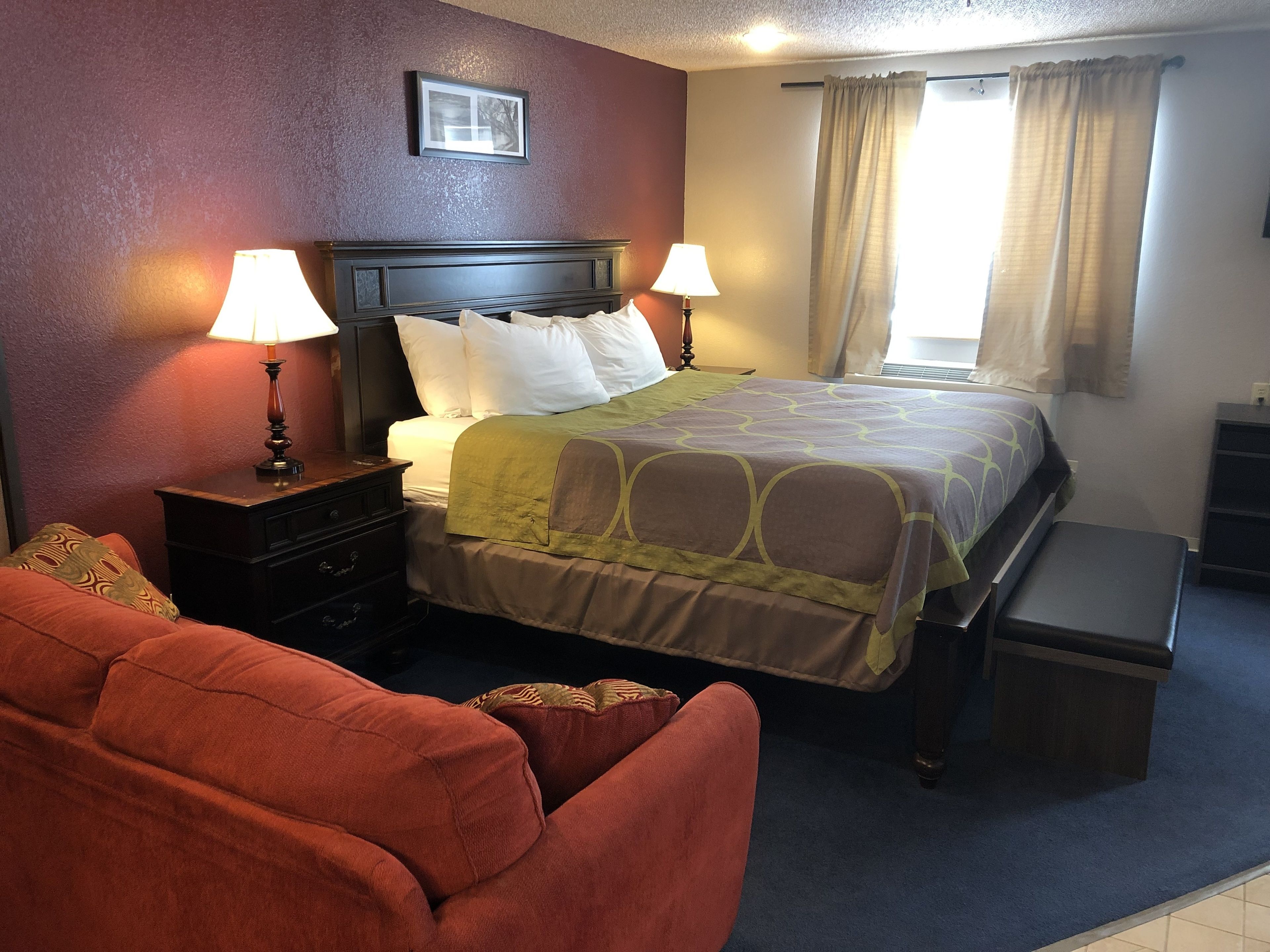 A neatly arranged hotel room with a bed, two bedside lamps, a nightstand, a bench, and a couch.
