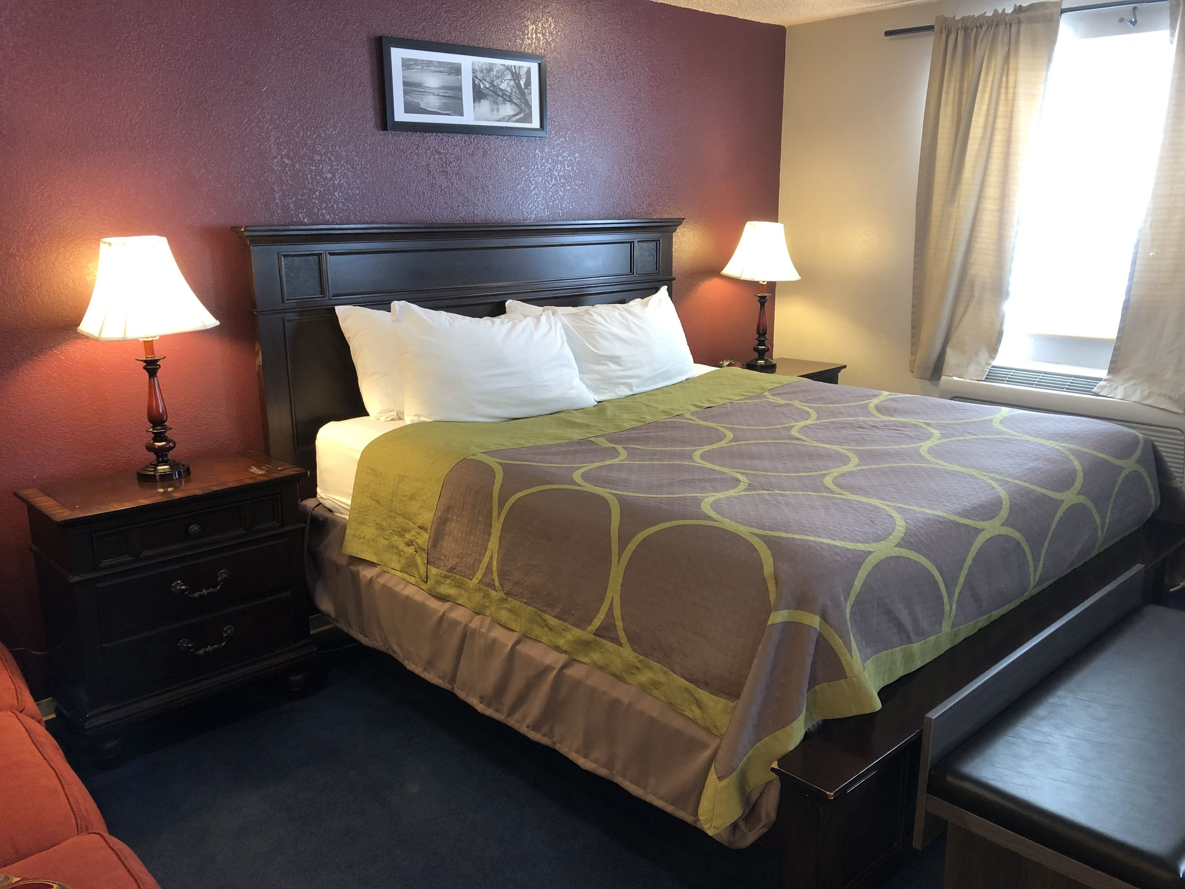 A neatly made bed with a patterned bedspread, two bedside lamps, a nightstand with drawers, and a framed picture on the wall.