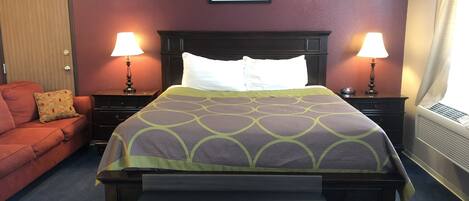 Une chambre d’hôtel avec un lit, des tables de chevet, un banc, un canapé rouge et un tableau au mur.