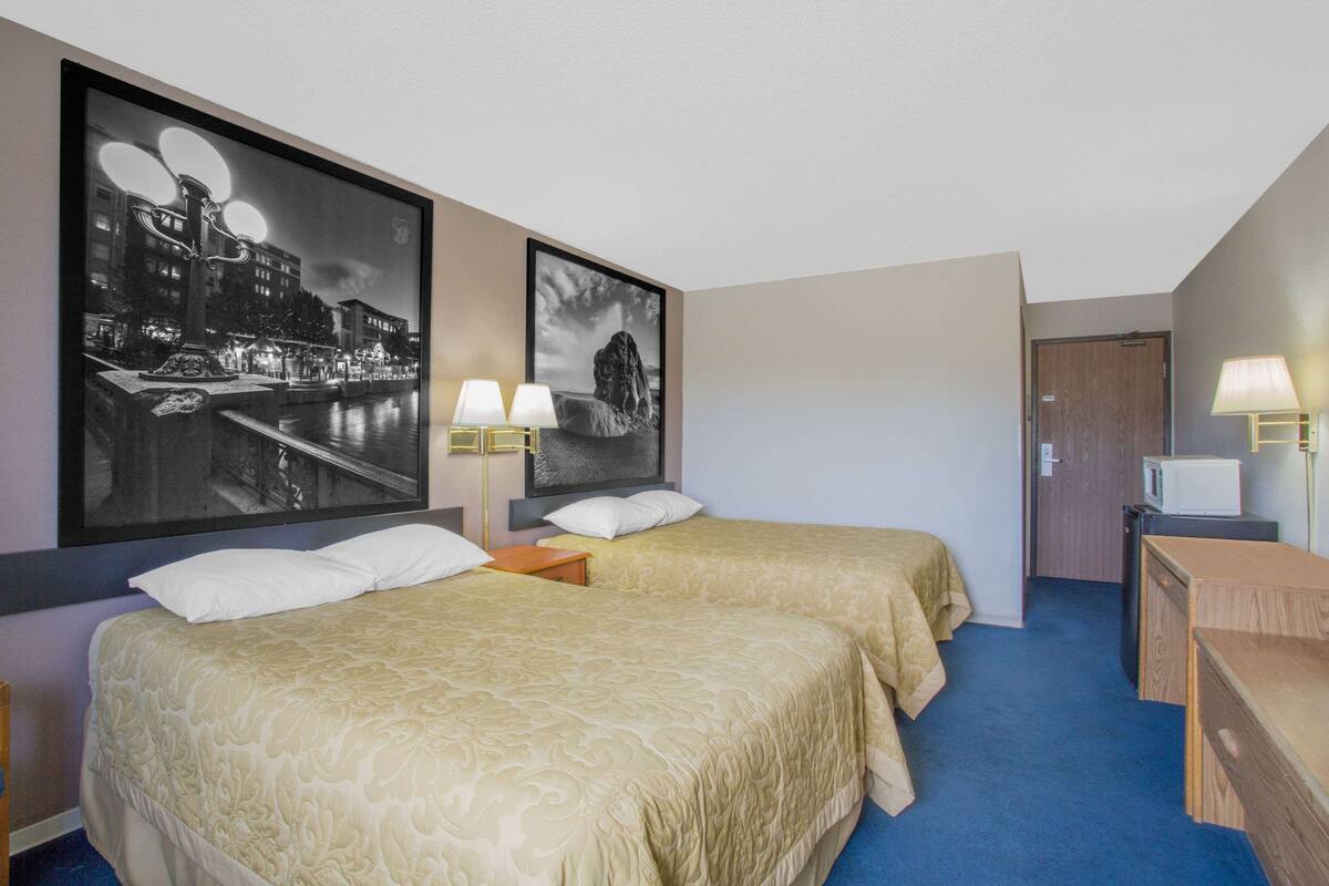 Une chambre d’hôtel avec deux lits, un bureau, une télévision et deux lampes fixées au mur.