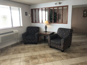 Une pièce comprenant deux fauteuils à motifs, une petite table avec une lampe, un radiateur et un grand miroir au mur.