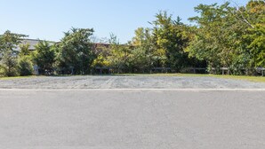 Un amplio estacionamiento con suelo de grava, rodeado de árboles y un edificio al fondo.