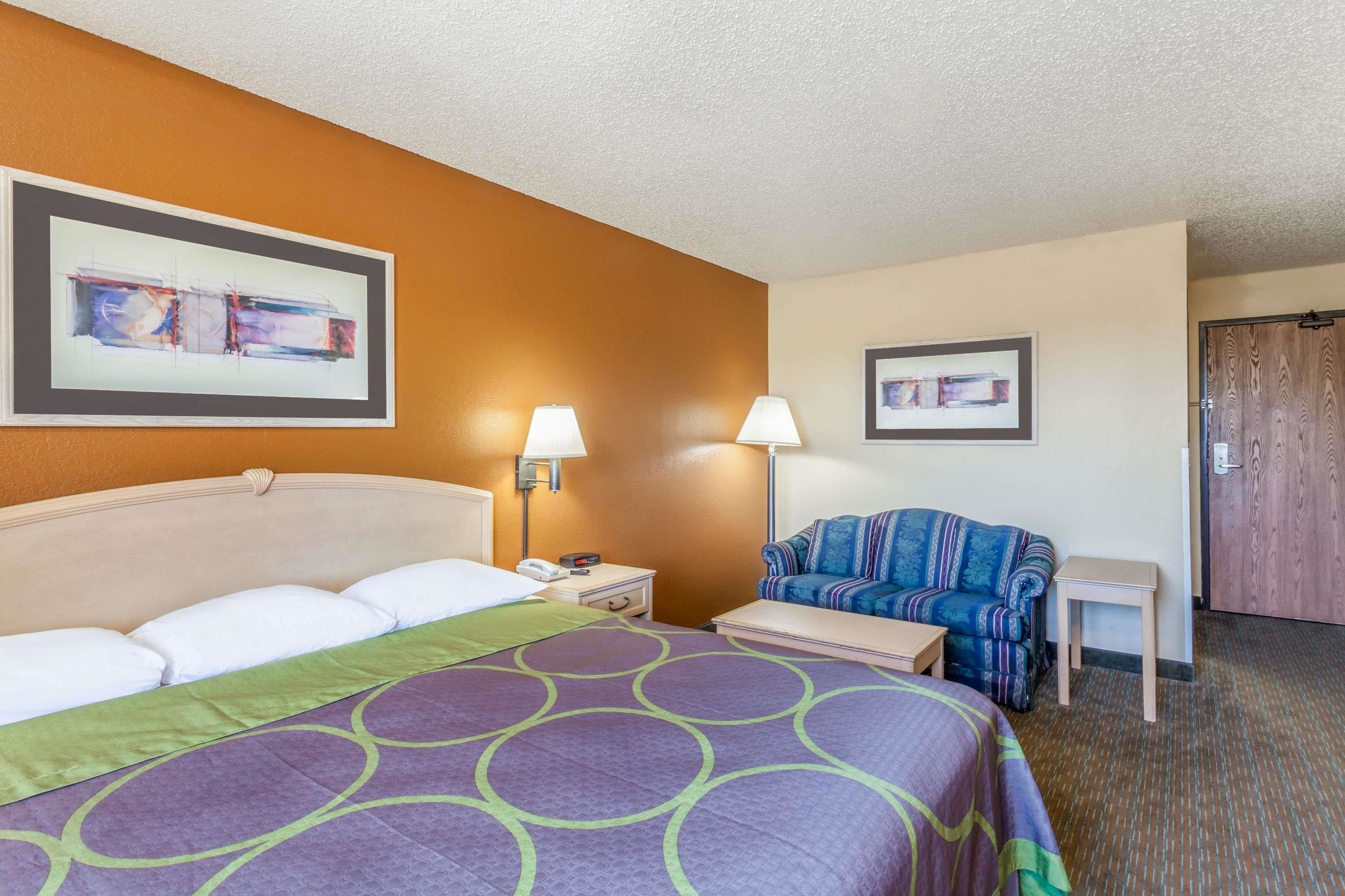Una habitación de hotel con una cama, dos mesitas de noche, un sofá y una puerta.